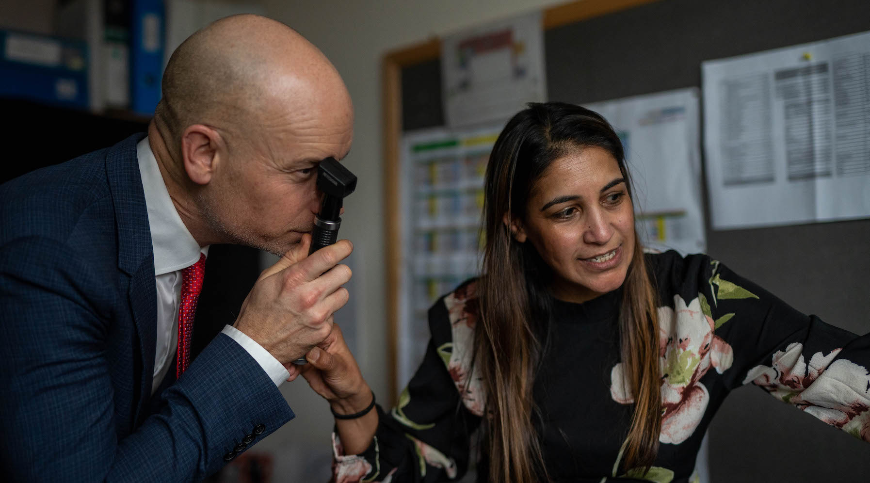 An optometrist shows Minister Kinnock how to test sight.