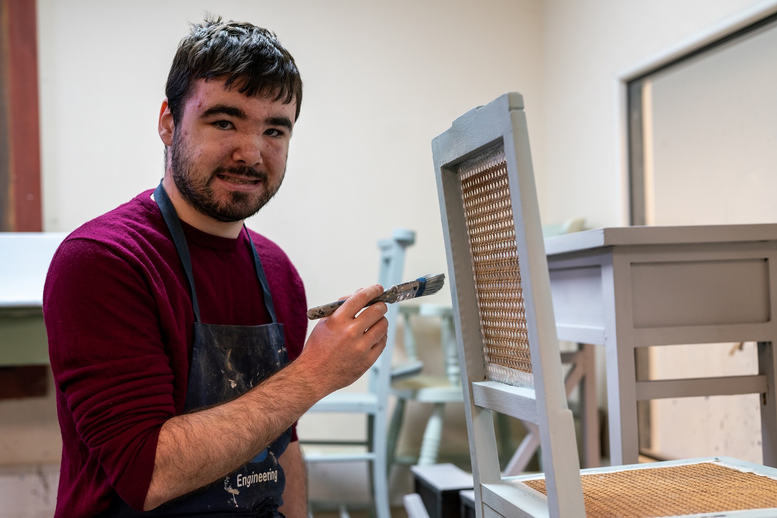 Ed smiles as he paints a chair in his woodwork workshop