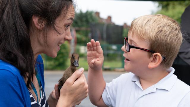 Nathan, a little boy in glasses, looks at a duckling held by a teacher