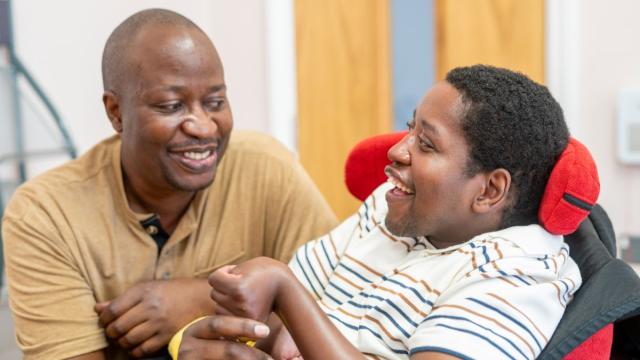 Sadick smiles in his wheelchair with his supporter